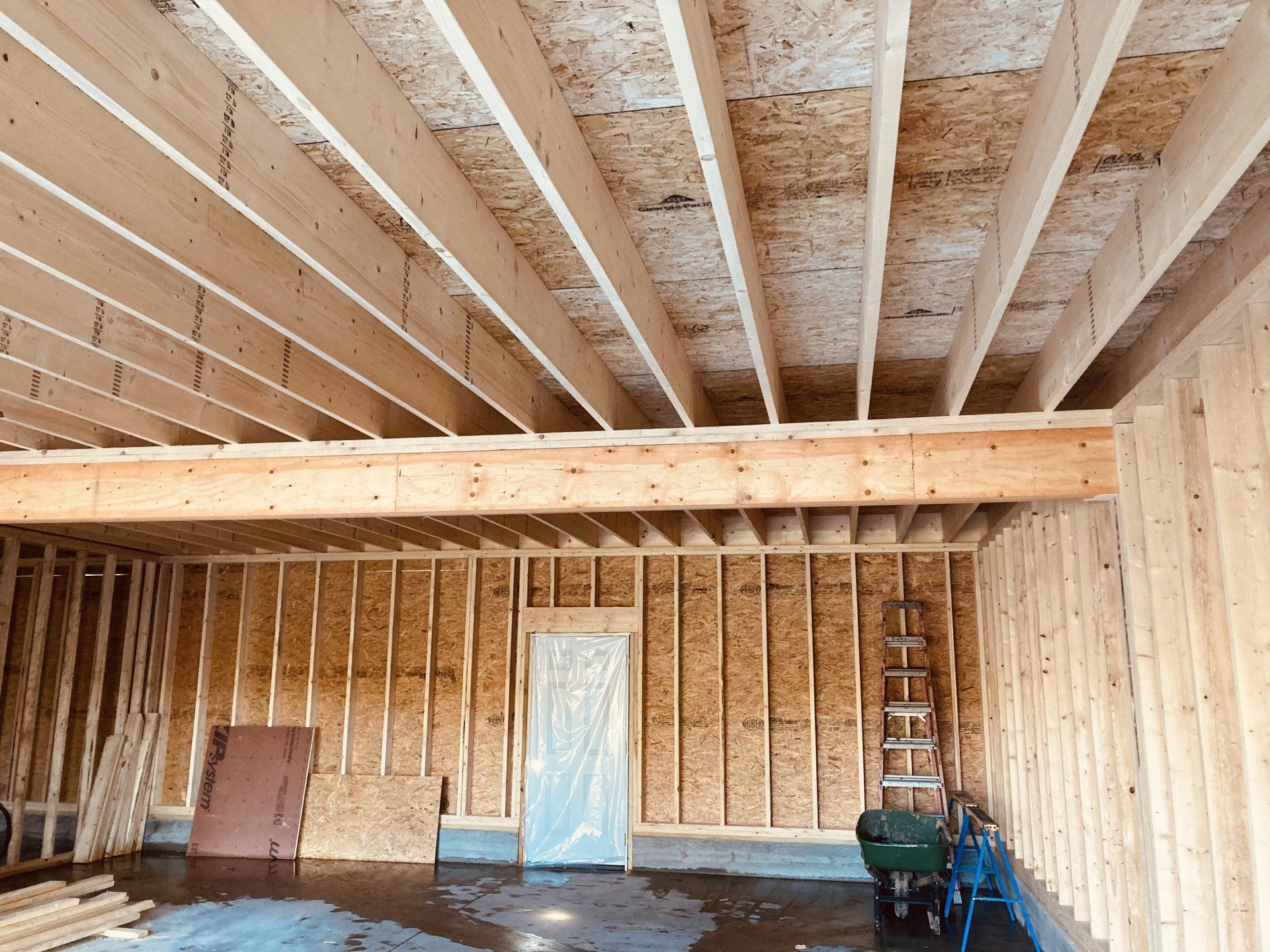A garage under construction with wooden beams and a green wheelbarrow.