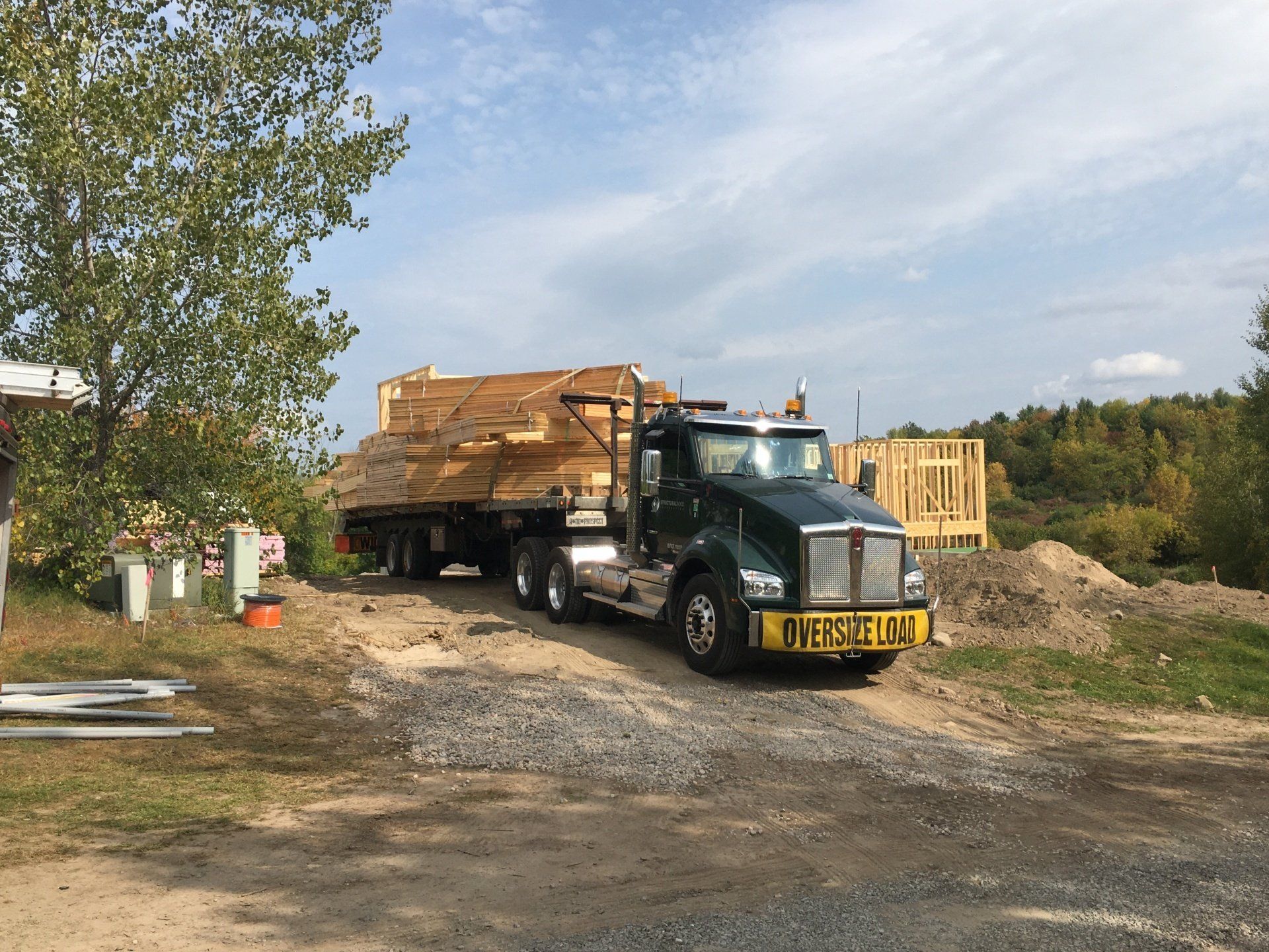 A truck is carrying a large load of wood on a dirt road.
