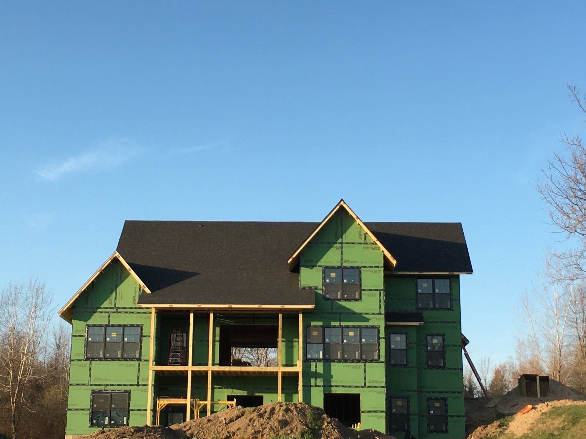 A large house under construction with green siding and a black roof