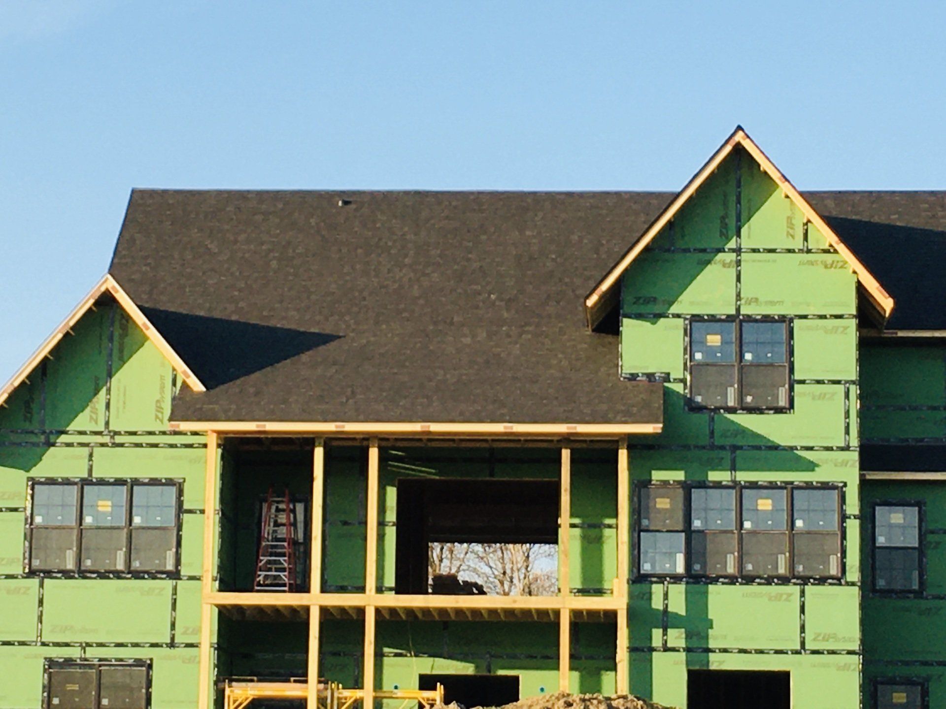 A large house is being built with green siding and a black roof