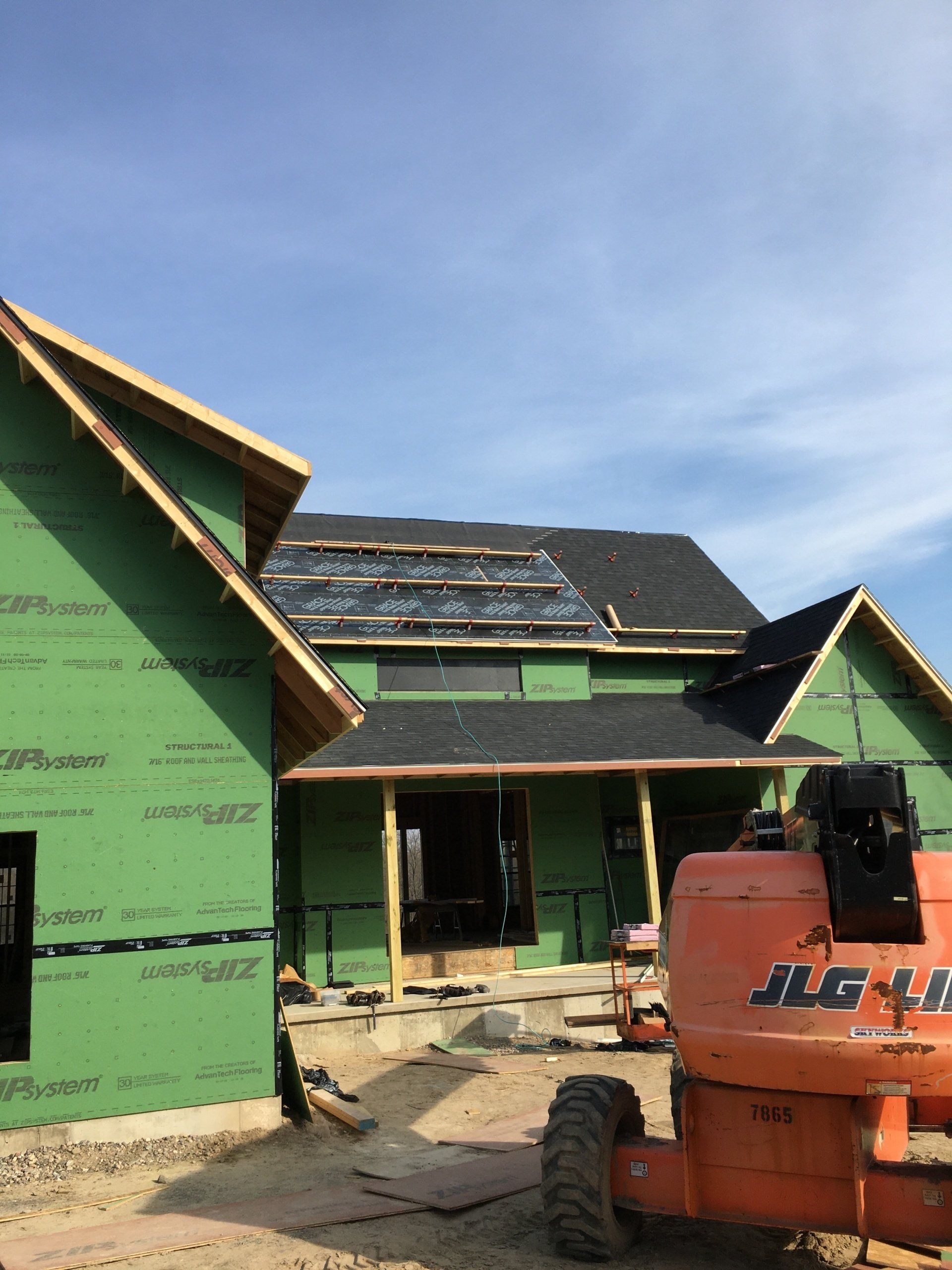 An orange jlg lift is parked in front of a house under construction.