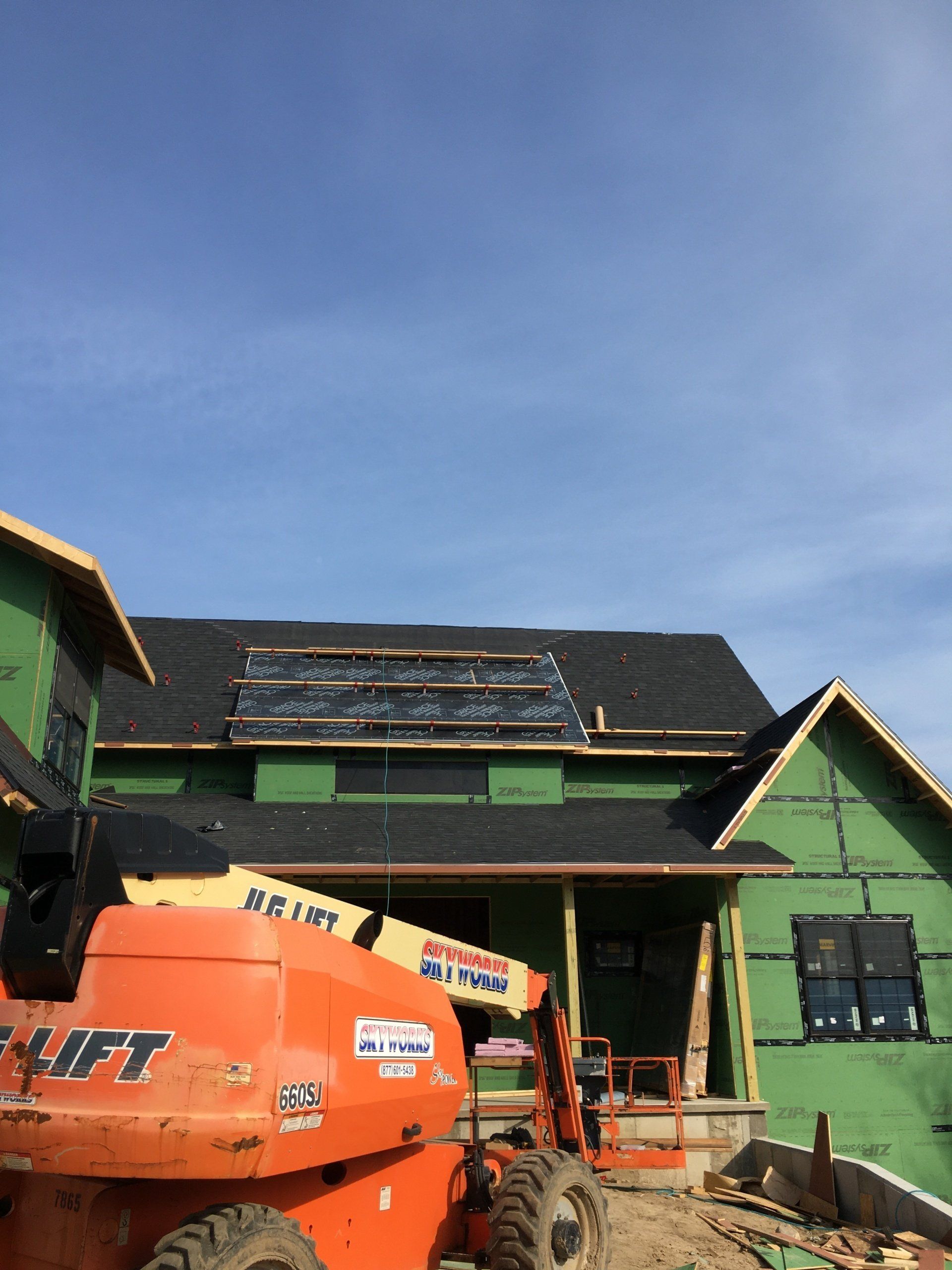 An orange lift is parked in front of a house under construction.