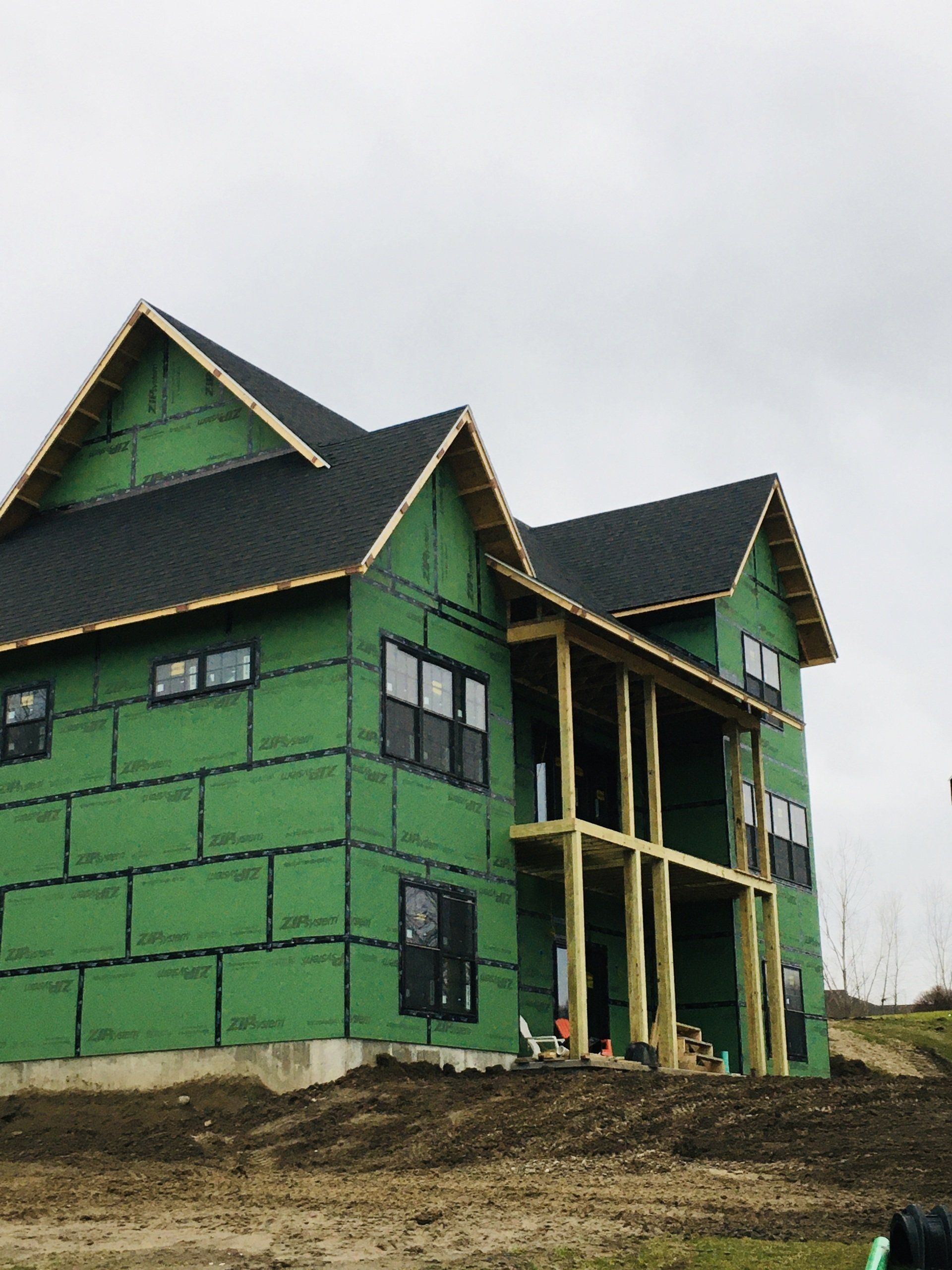 A large house is being built with green siding and a black roof.