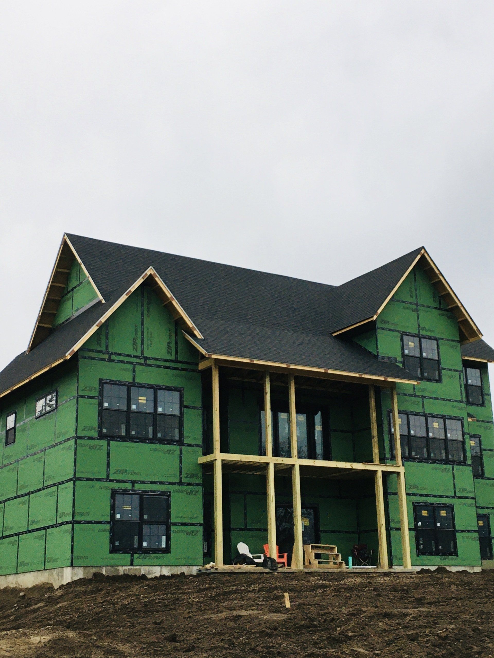 A large house is being built with green insulation and a black roof.