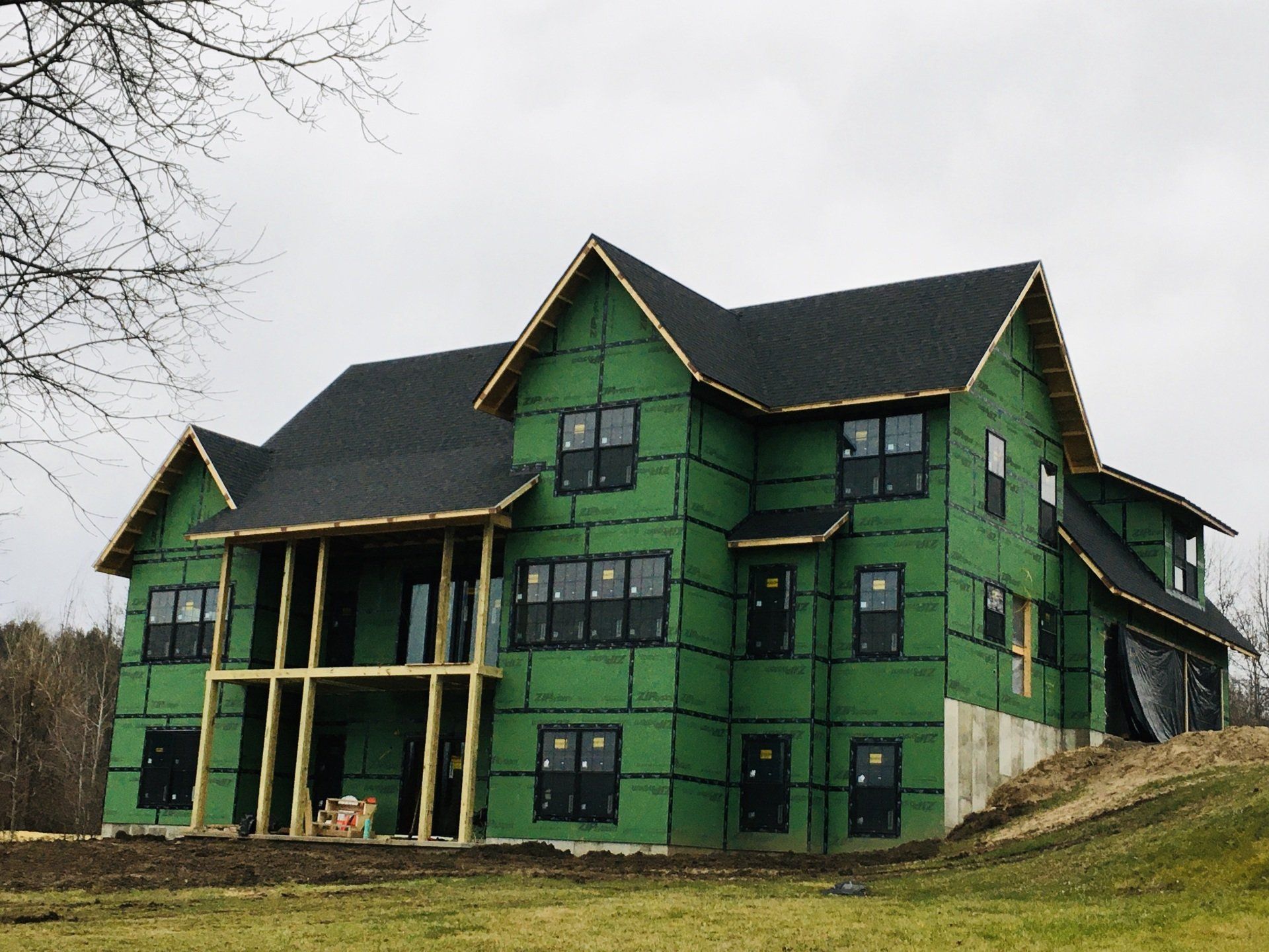 A large house is being built with green siding and a black roof.