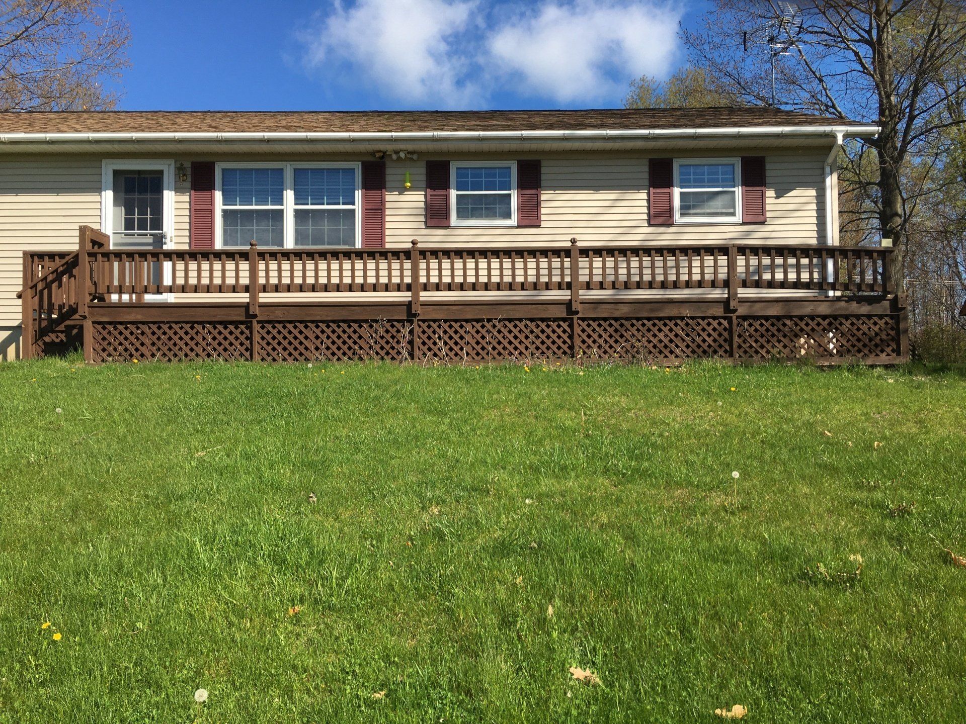A mobile home with a large deck is sitting on top of a lush green field.