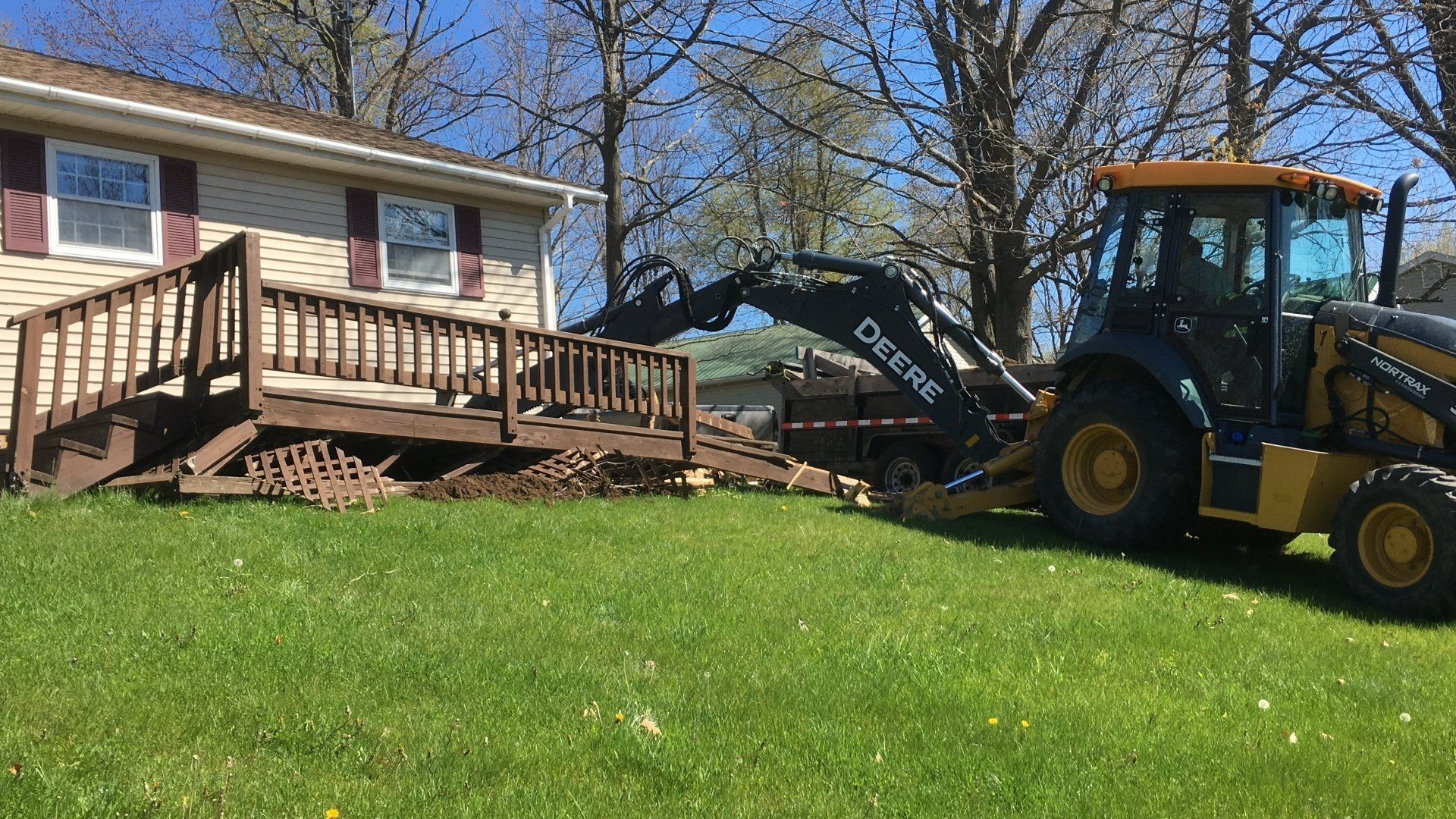 A tractor is moving a wooden deck in front of a house.