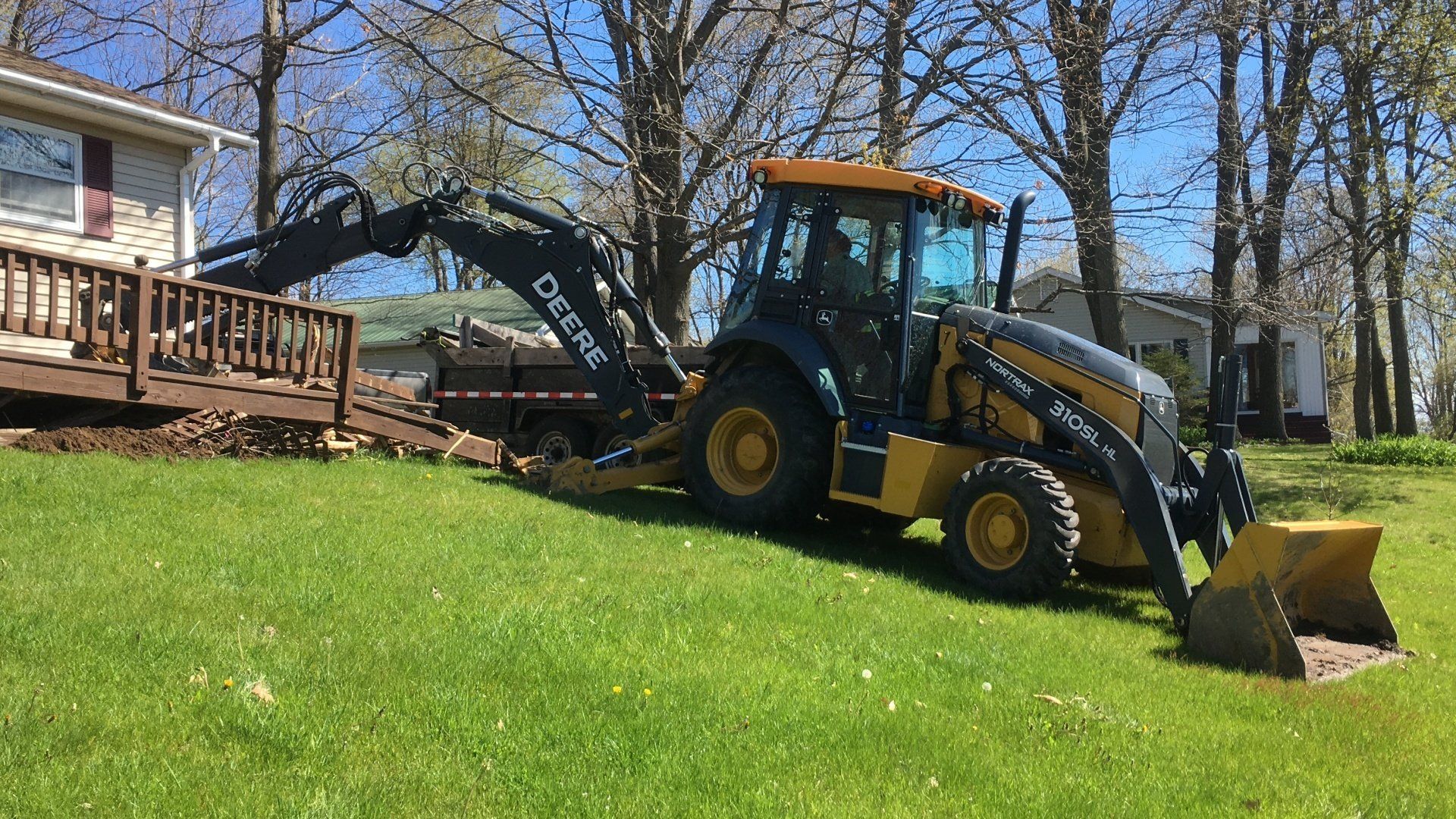 A tractor is digging a hole in the grass in front of a house.