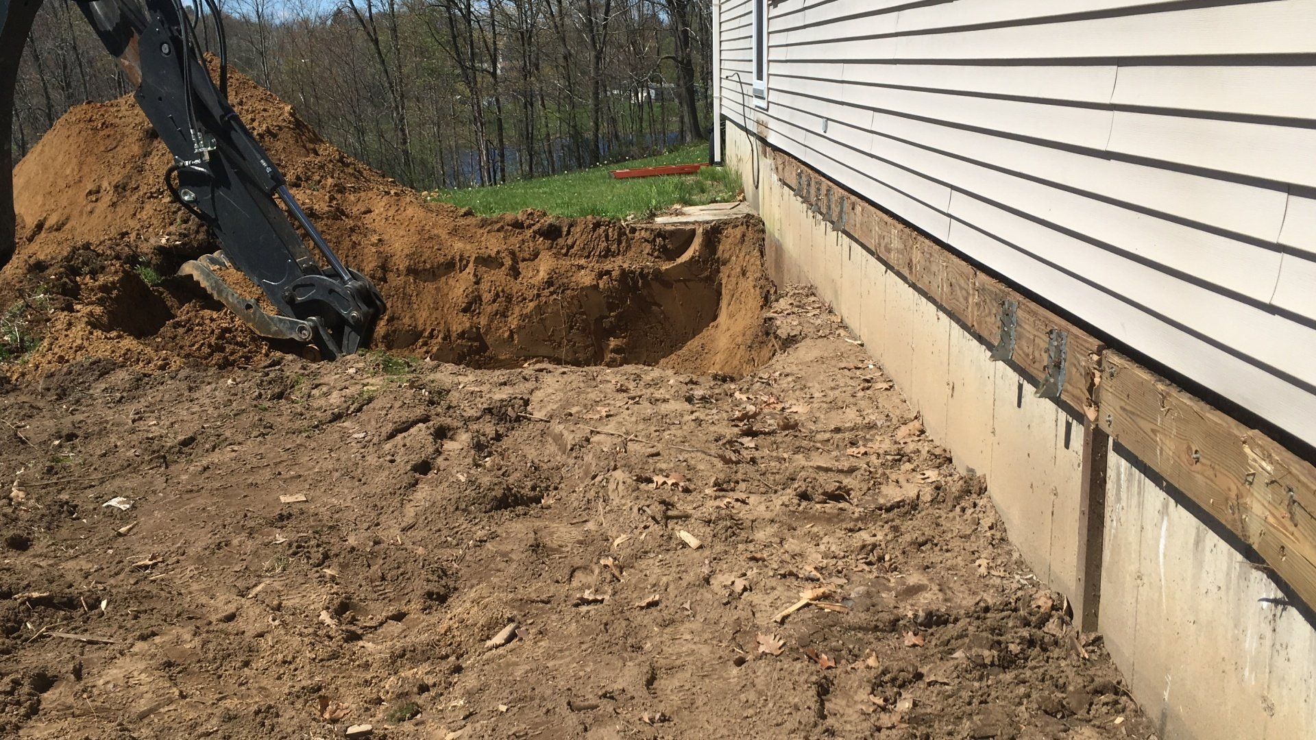 An excavator is digging a hole in the ground in front of a house.
