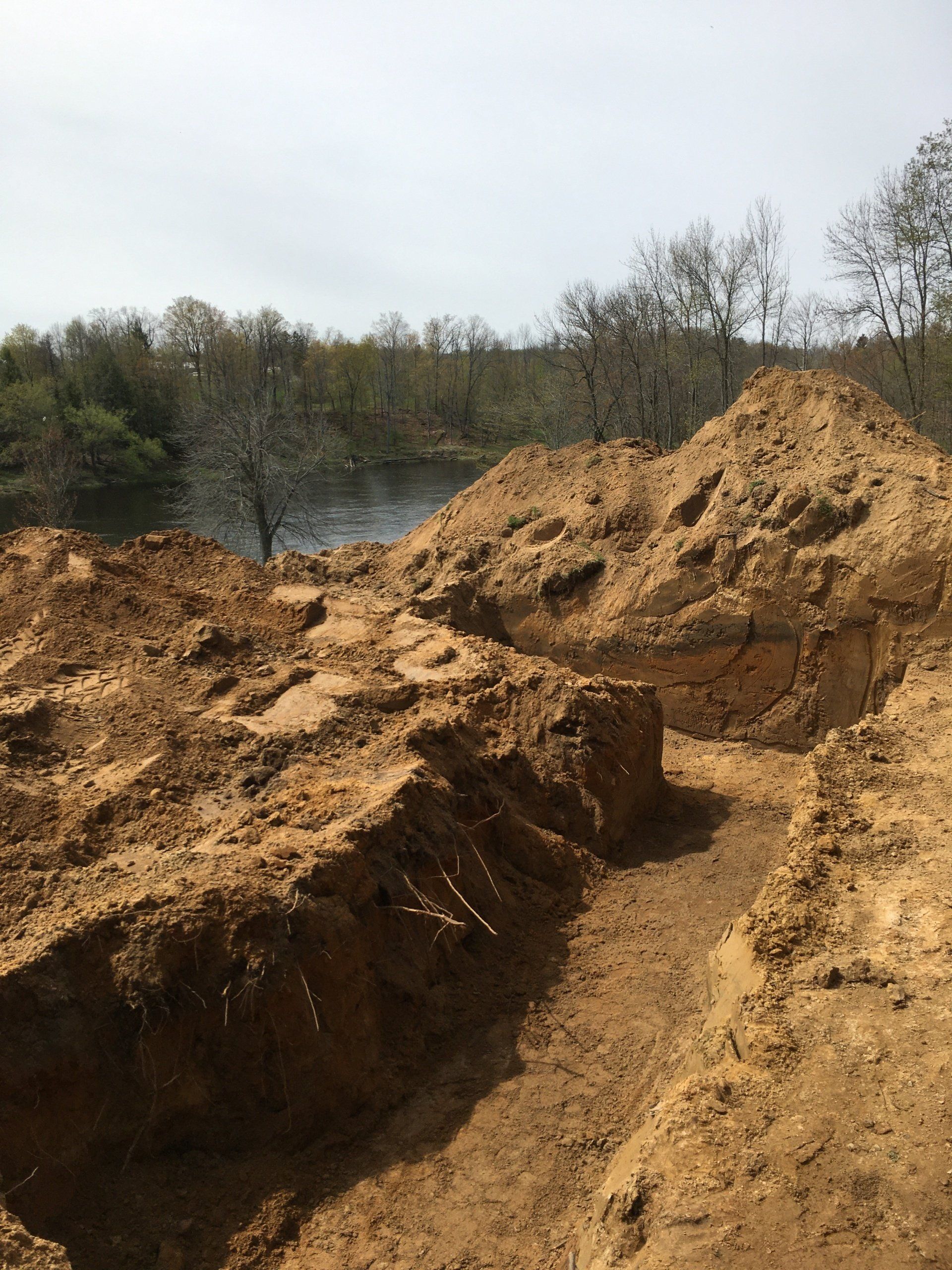 A pile of dirt is sitting next to a body of water.