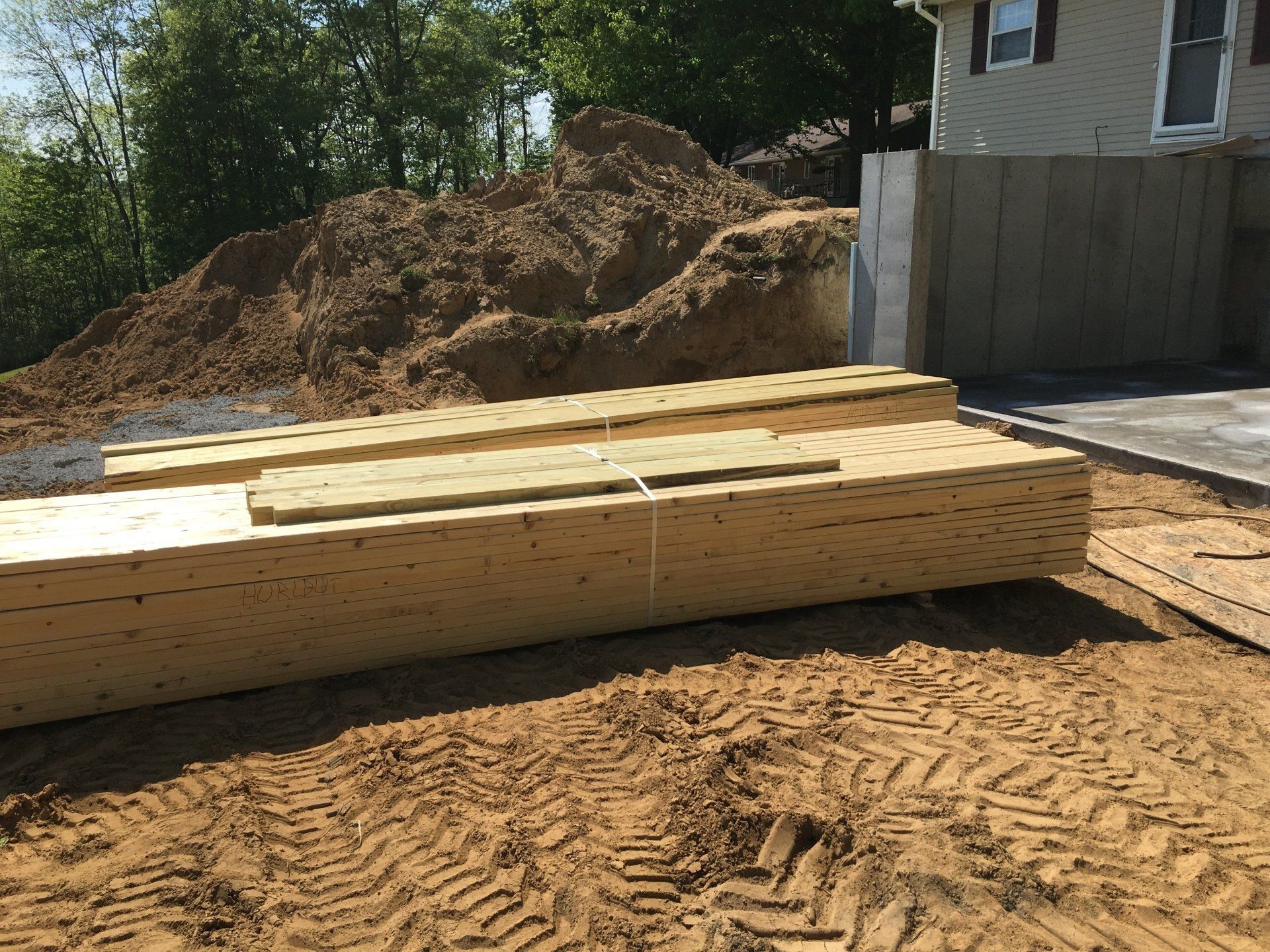 A pile of wood is sitting in the dirt in front of a house.