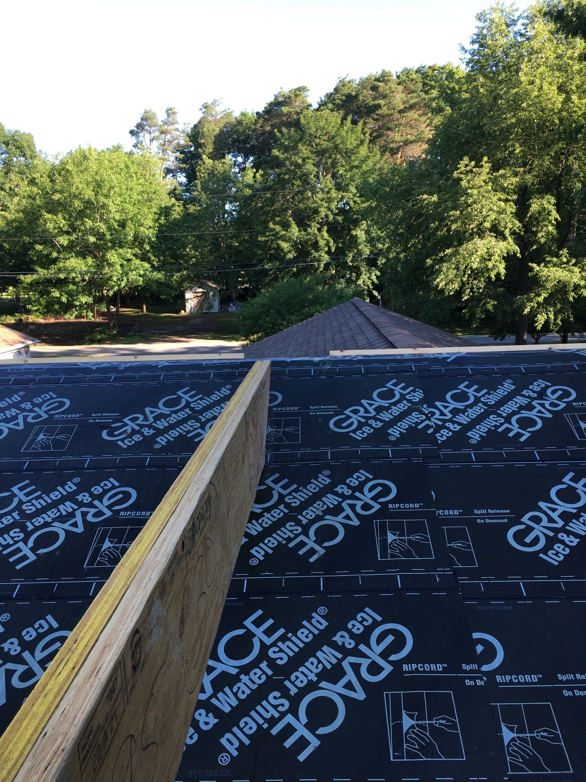 A wooden beam is sitting on top of a black roof with trees in the background.