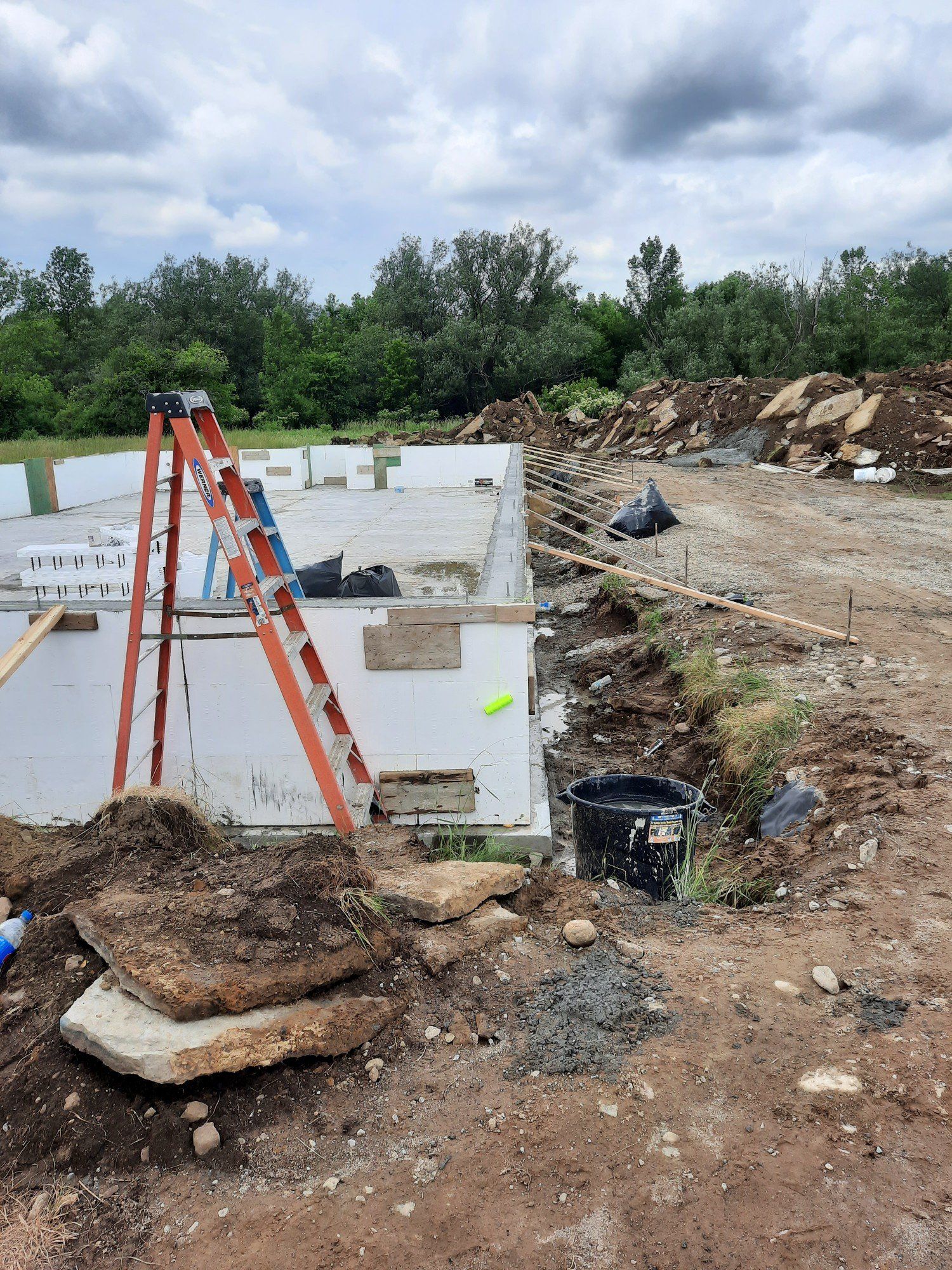 A ladder is sitting in the dirt in front of a building under construction.