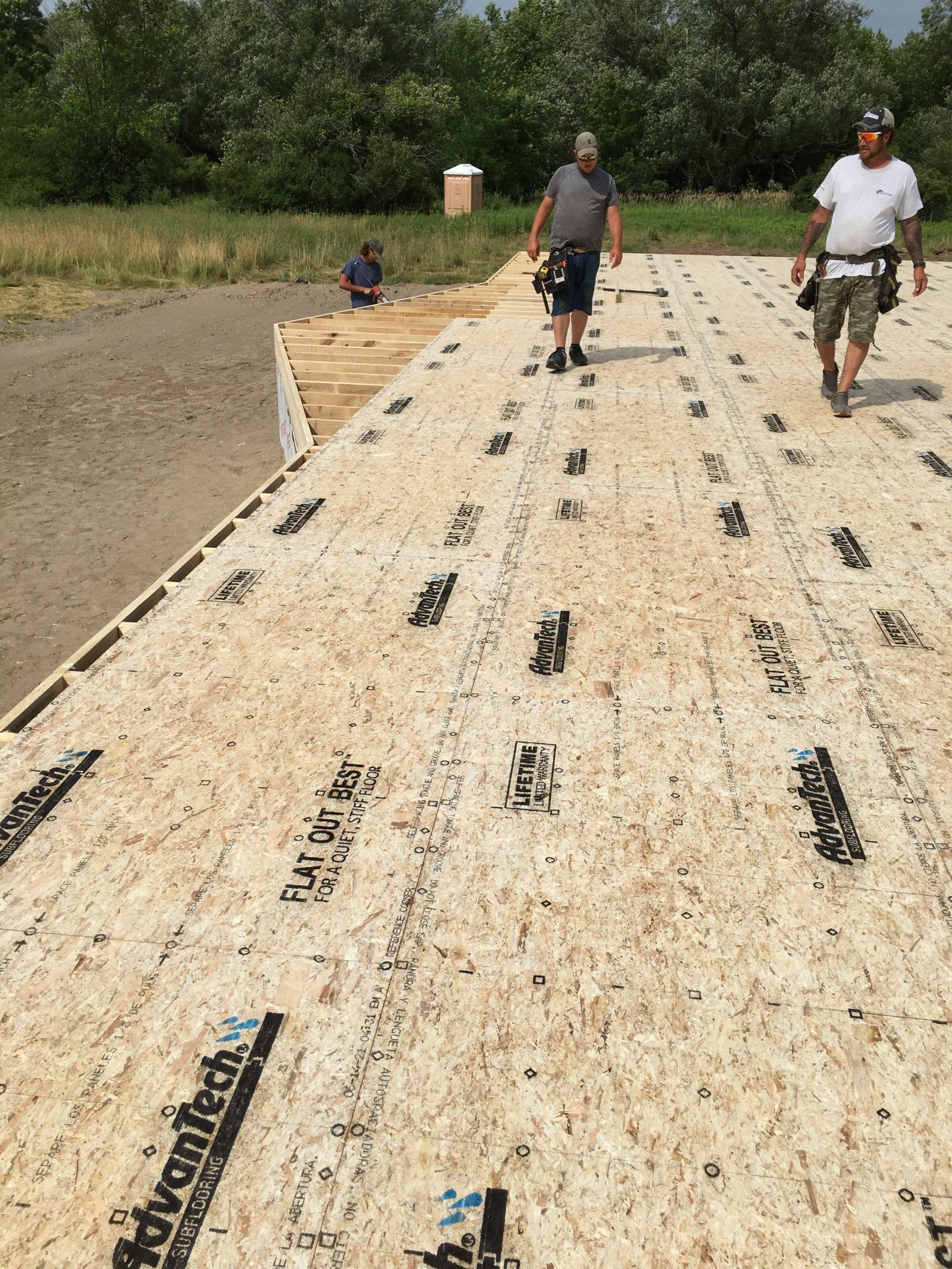 Two men are walking on top of a large piece of plywood.