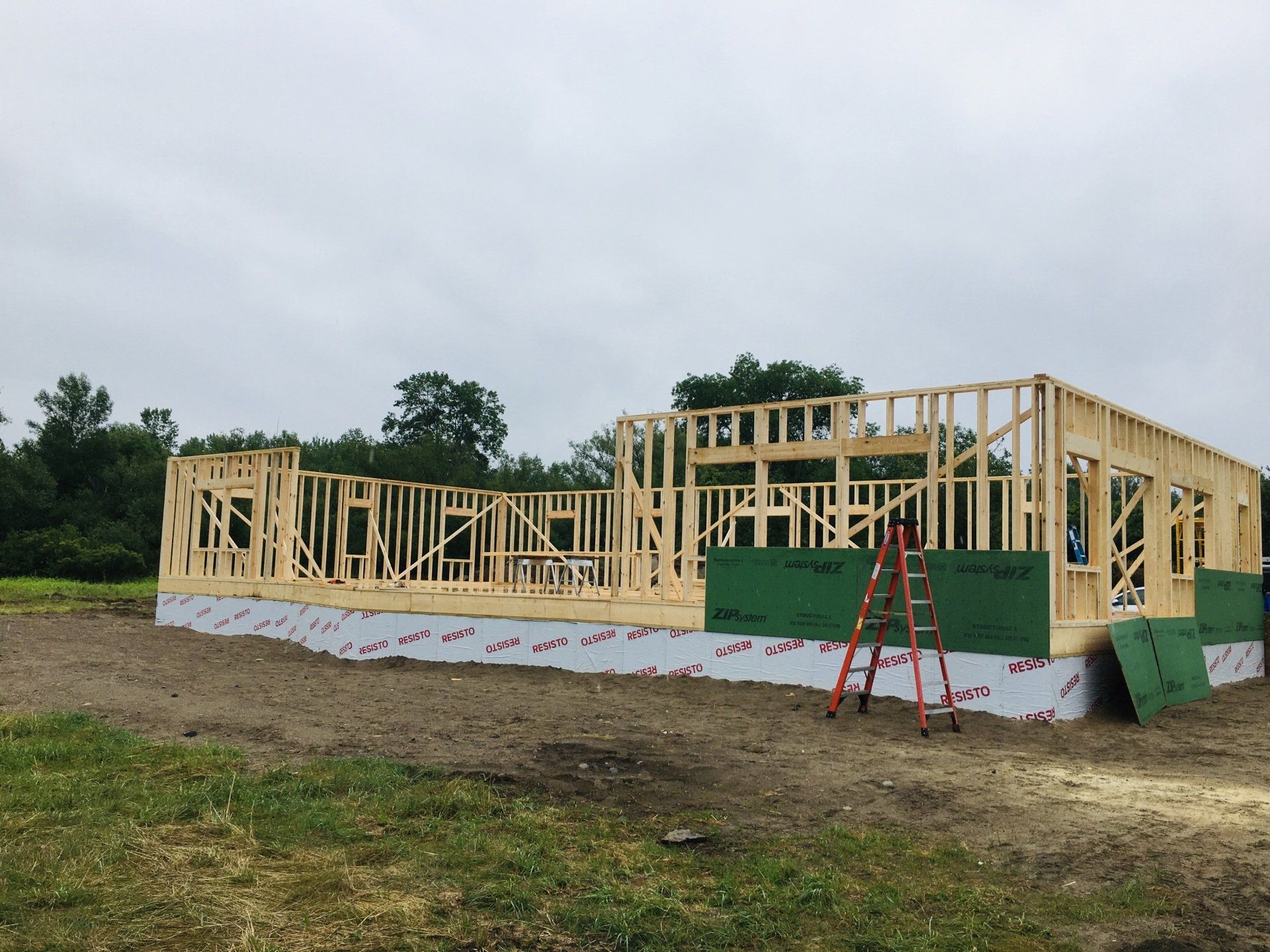 A house is being built in a field with a ladder in the foreground.