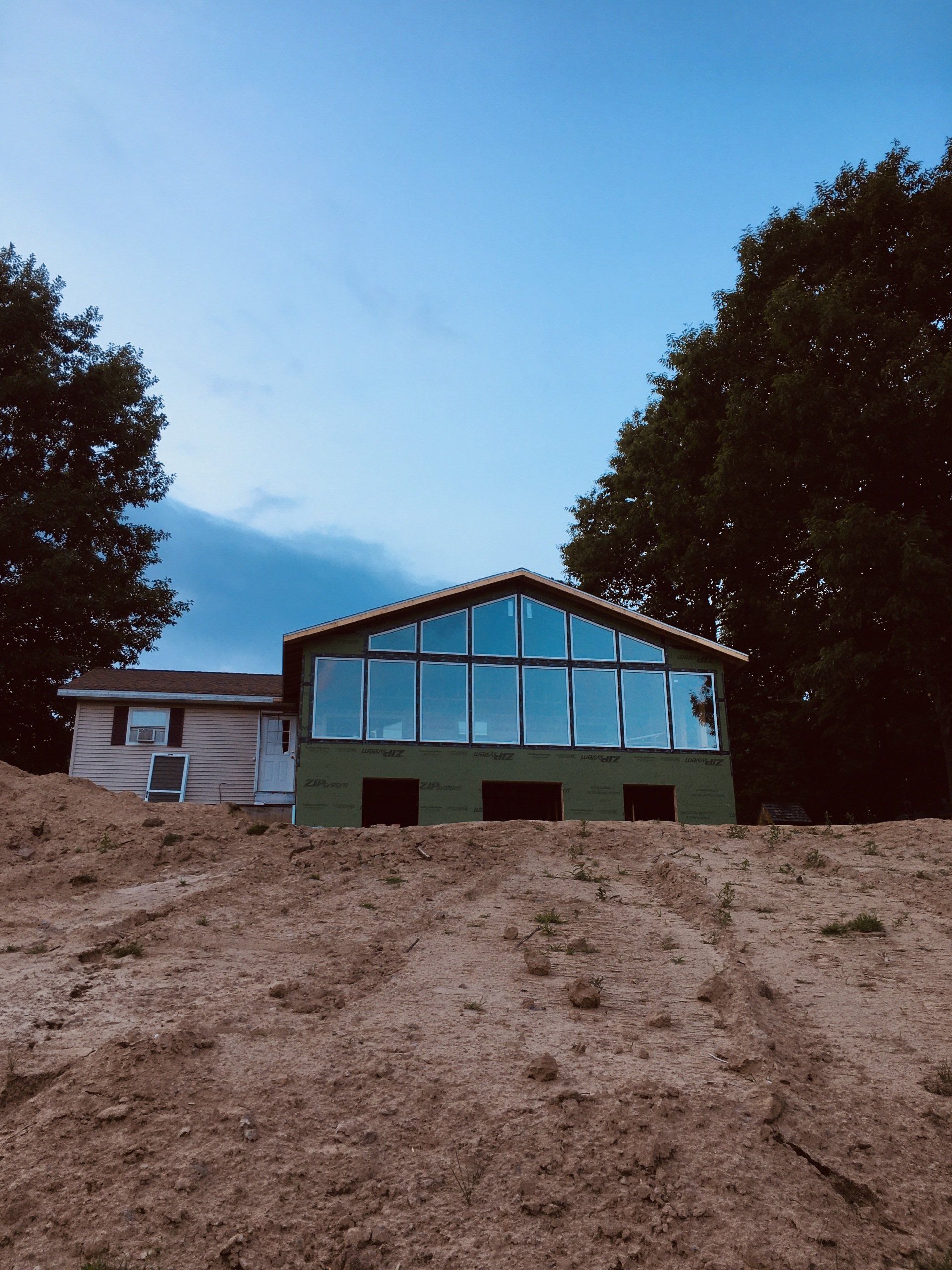 A house with a lot of windows sits on top of a dirt hill