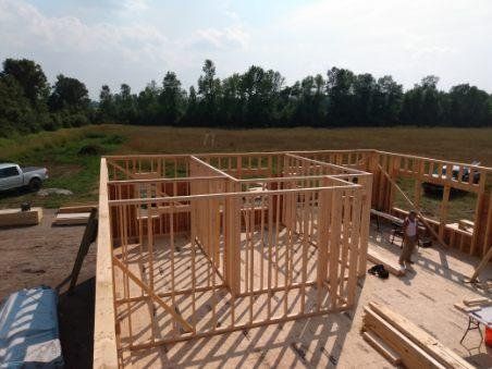 A house is being built in a field with a truck parked in the background.