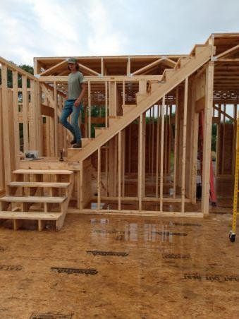 A man is standing on top of a wooden staircase in a house under construction.