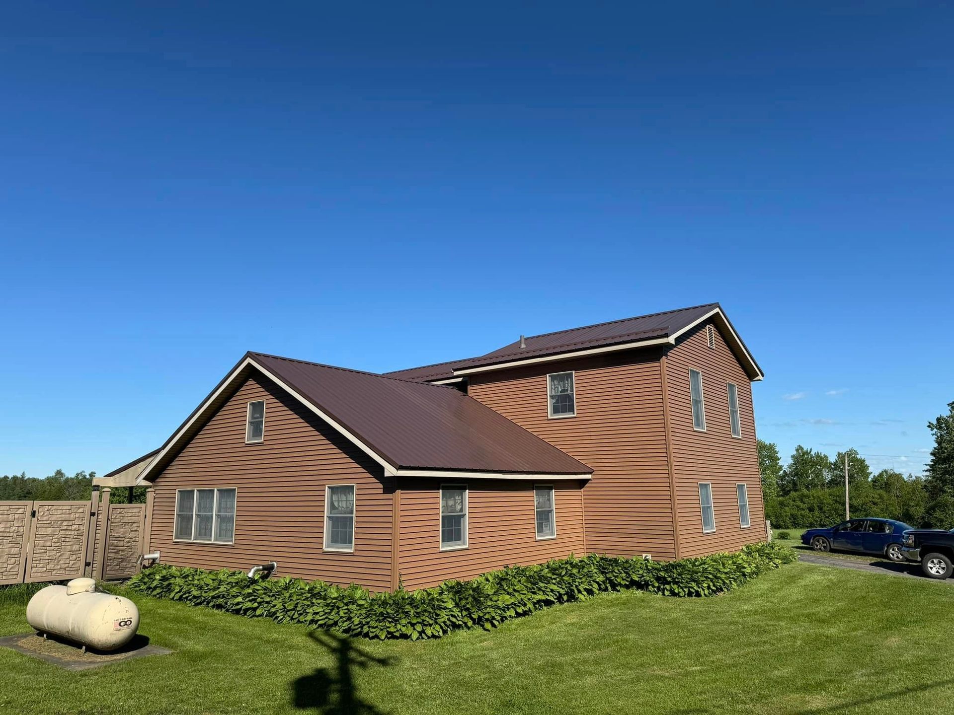 A large brown house with a propane tank in front of it.