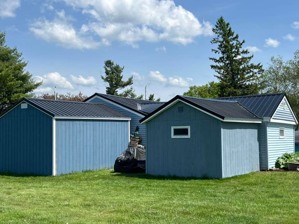 A group of blue sheds are sitting next to each other in a grassy yard.
