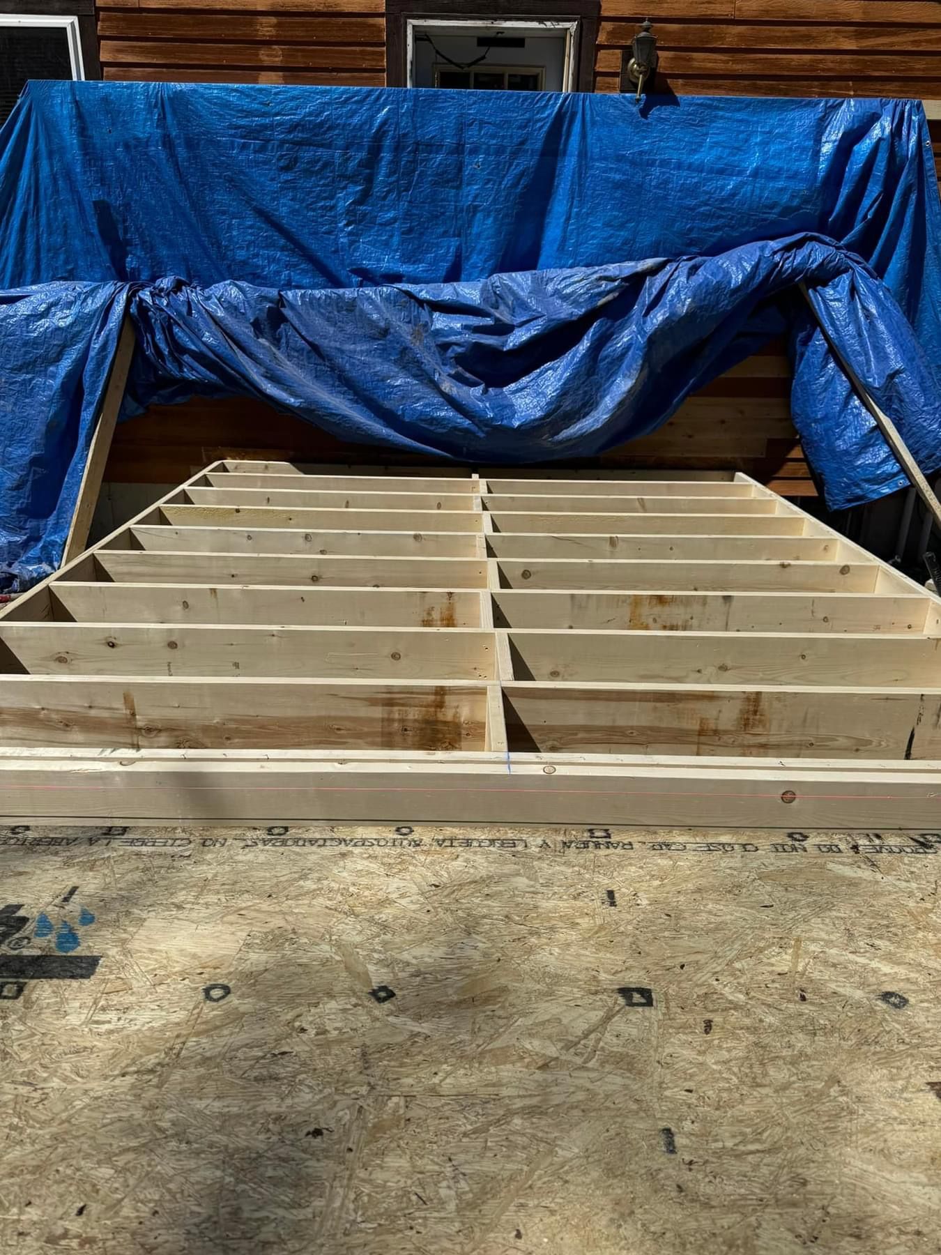 A wooden frame is sitting on top of a concrete floor next to a blue tarp.