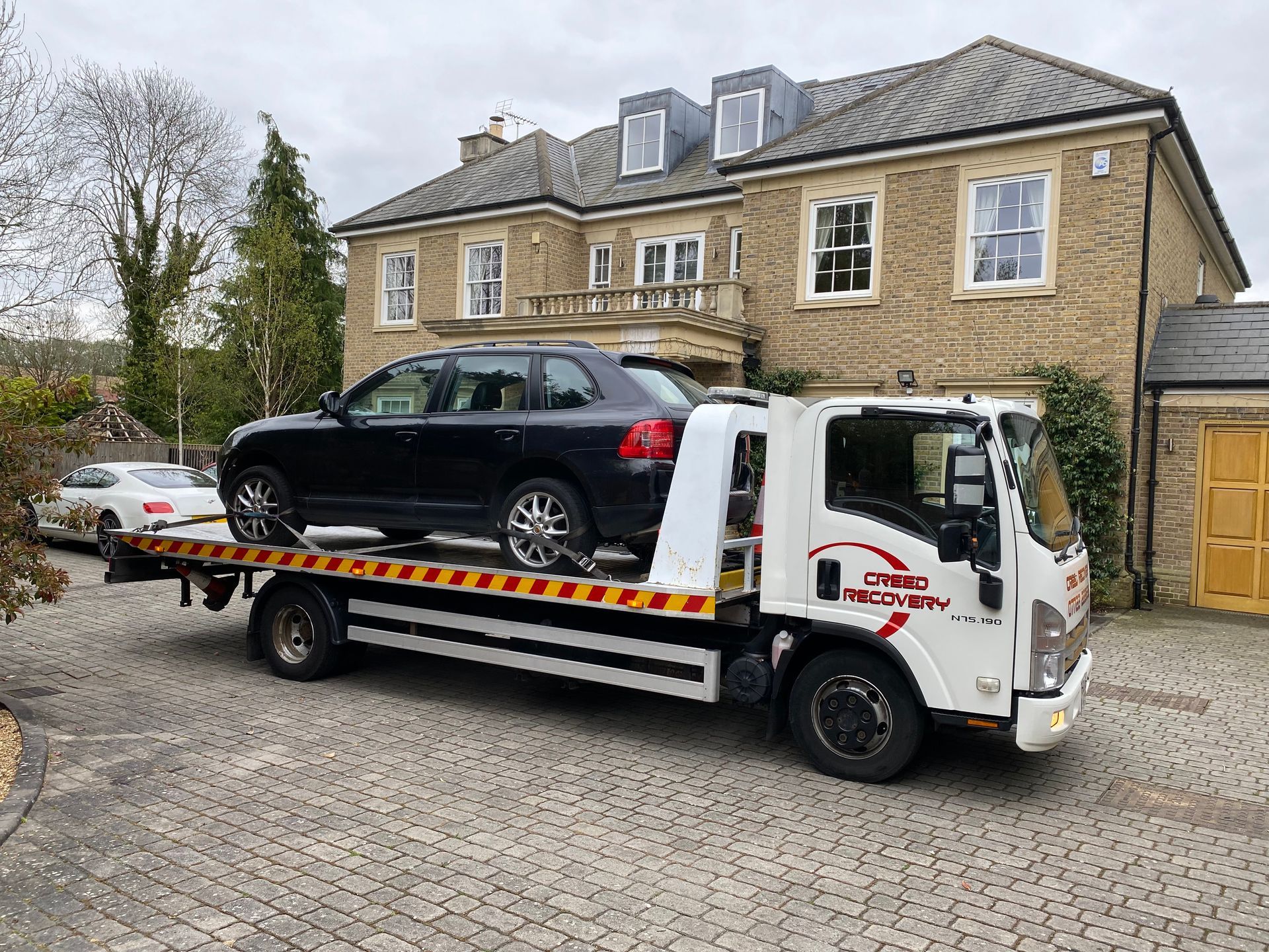 A tow truck is towing a car in front of a large house.