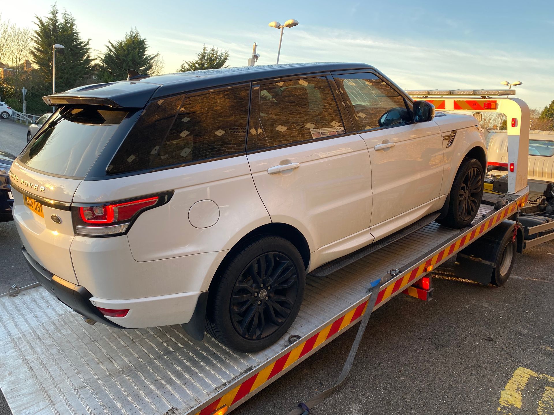 A white range rover sport is being towed by a tow truck.