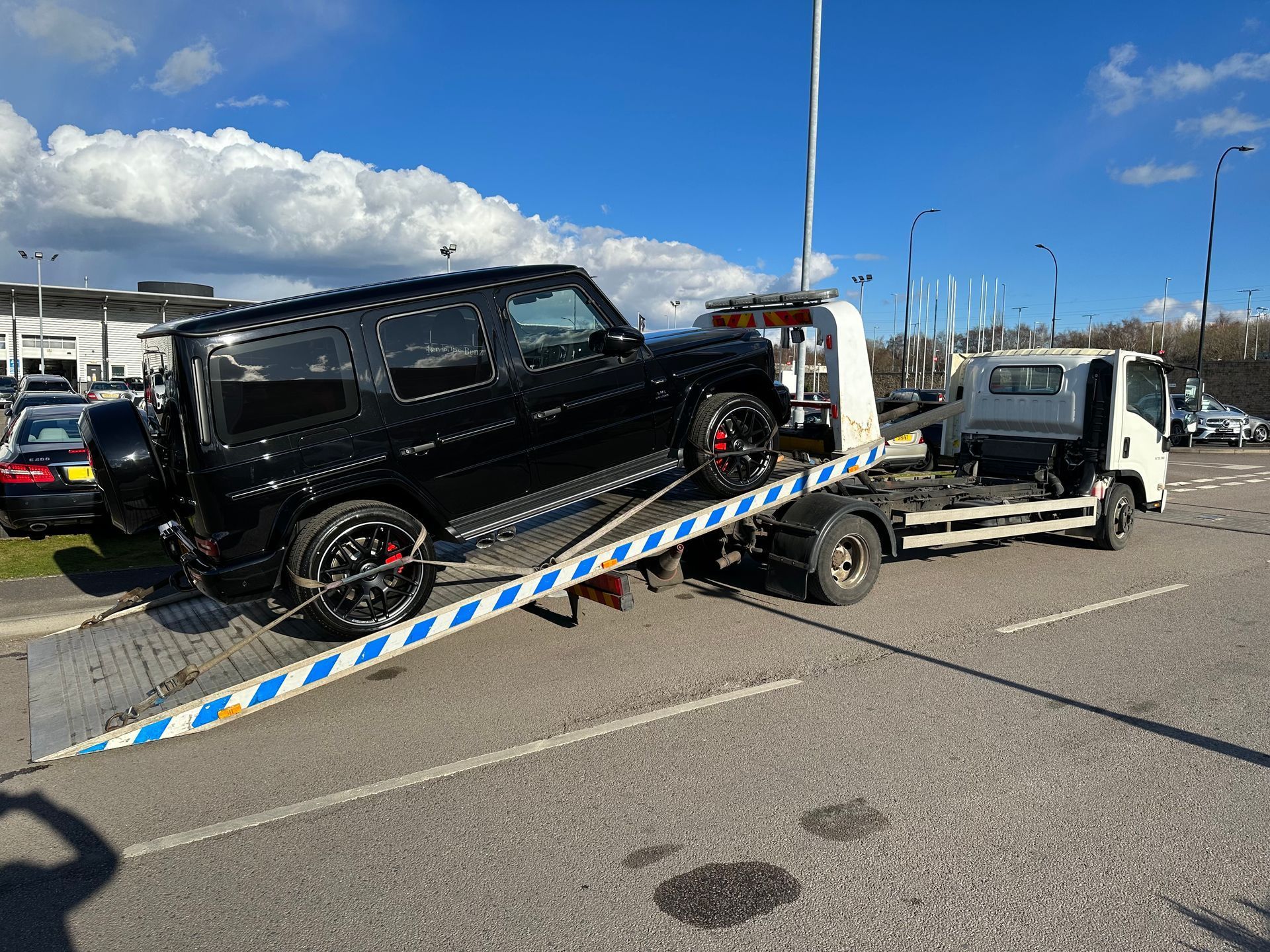 A tow truck is carrying a black suv on the back of it.