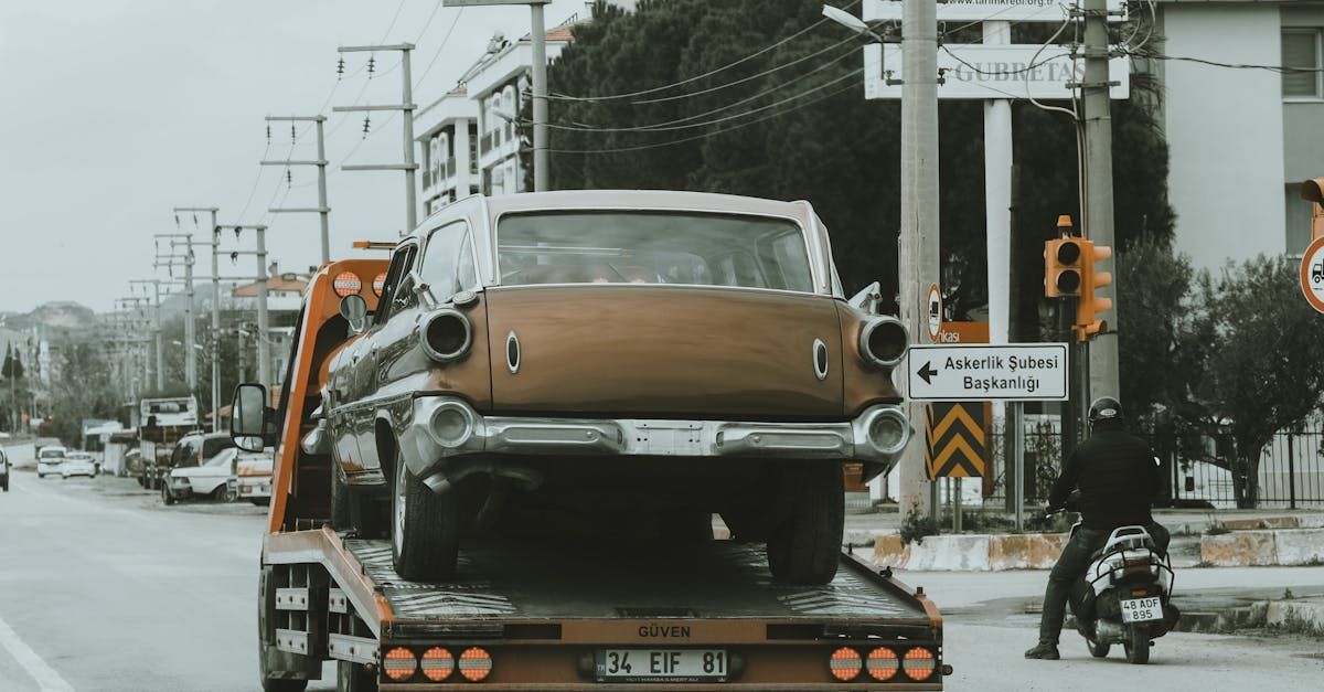 An old car is being towed down a street by a tow truck.