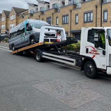 A tow truck is towing a van down a street.