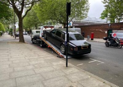 A black car is being towed down a street by a tow truck.