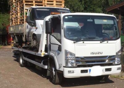 A white isuzu tow truck is carrying a car on the back of it.