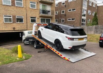 A white range rover is being towed by a tow truck.