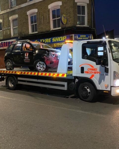 A tow truck with a car on the back is parked in front of a tyre shop