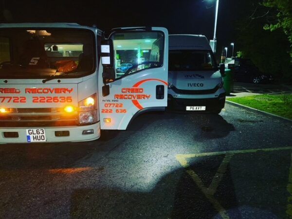 A recovery truck is parked next to another truck