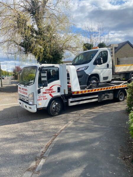 A tow truck with a van on the back is parked on the side of the road.