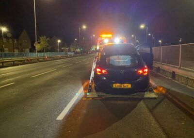 A car is being towed down a highway at night.