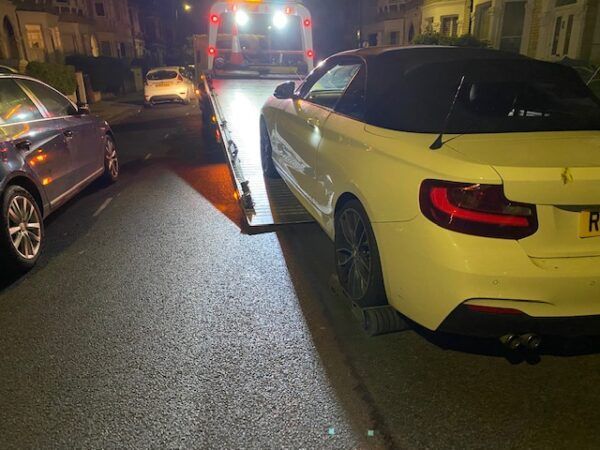 A white car is being towed by a tow truck.