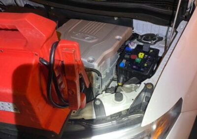 A red jump starter is plugged into the engine of a white car.