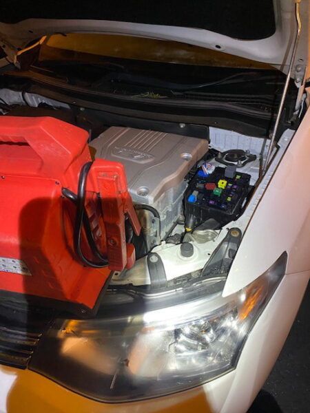 A white car with the hood open and a red battery.