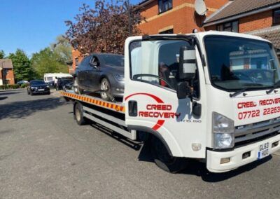 A tow truck with a car on the back is parked on the side of the road.