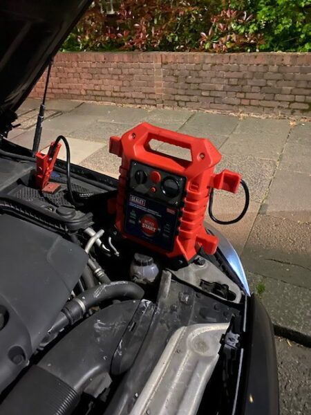 A red jump starter is sitting under the hood of a car.