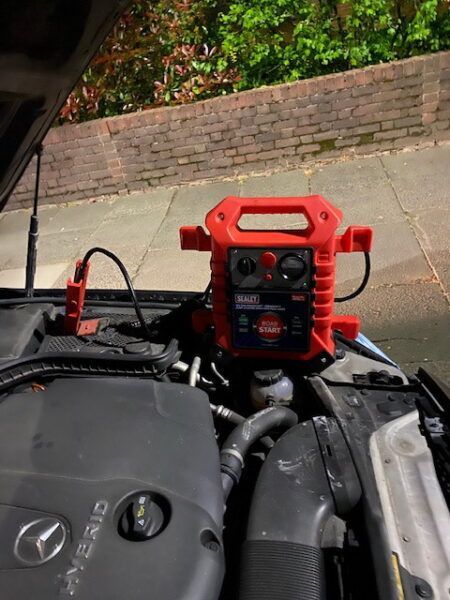A red jump starter is sitting under the hood of a car.