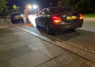 A car is being towed down the street by a tow truck at night.