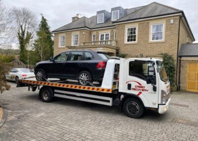A tow truck is towing a car in front of a large house.