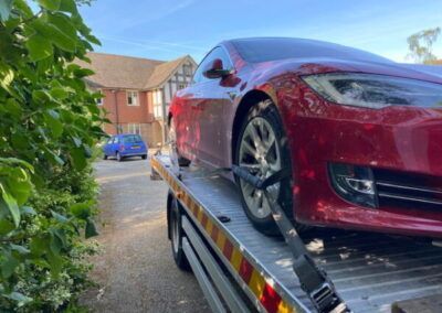 A red tesla model s is being towed by a tow truck.