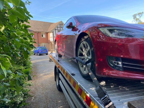 A red tesla model s is being towed by a tow truck.
