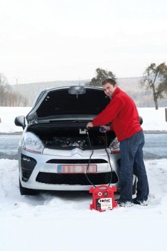 A man is standing next to a car with the hood up in the snow.