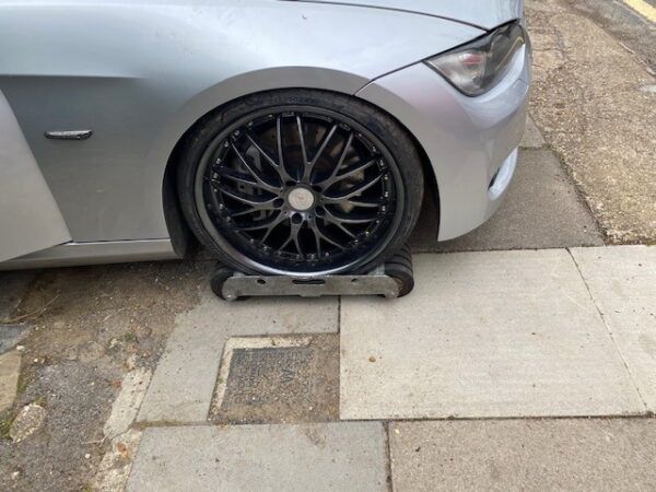 A silver car with black wheels is parked on a sidewalk