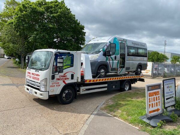 A tow truck is carrying a van down a street.